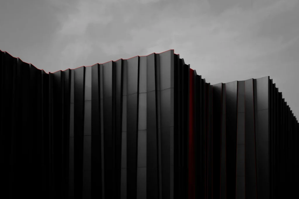 Modern black building facade with vertical panels under cloudy sky.